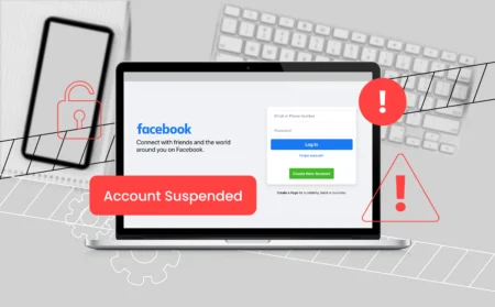 A laptop screen displaying a locked Facebook login page with a red warning triangle and the word 'Account Suspended' when you are banned from Facebook. The surrounding workspace includes a phone and notepad.